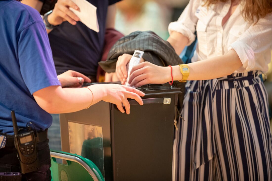 A young person is putting a ballot paper into a ballot box being held by an SYP staff member