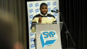 SYP77 Board Member Crisantos Ike on stage at SYP77