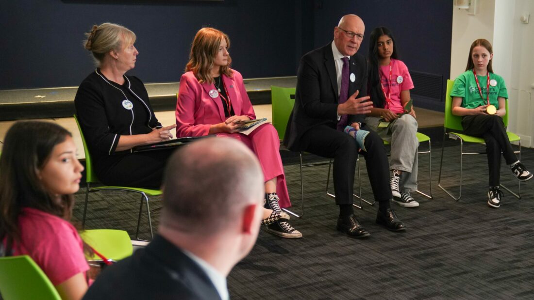 First Minister John Swinney speaking at the Annual Cabinet Meeting with Children and Young People in November 2024 with young people and other Ministers sat next to him