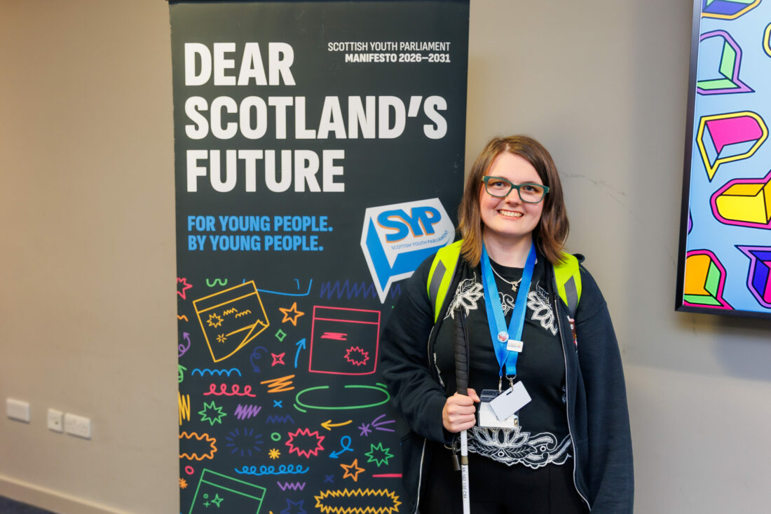 Eilidh Morrison MSYP posing next to a poster which says Dear Scotland's Future - SYP manifesto.