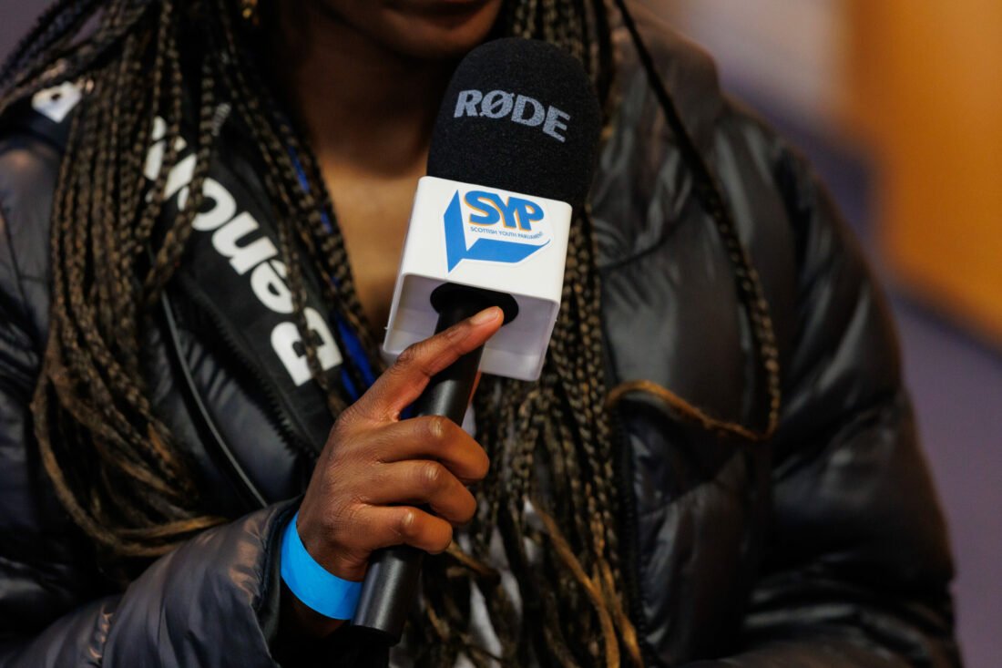 A young person of colour holding a microphone which has the SYP logo stamped on it.