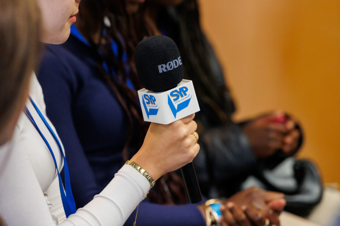 An MSYP holding a microphone with the SYP logo on it. Only her hand is visible.
